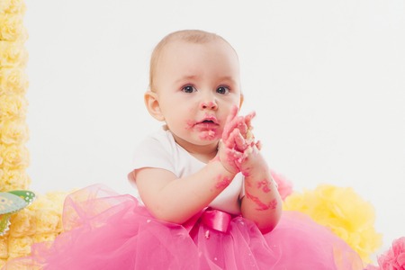a little girl eats cake with her hands. The baby was covered in food. isolated white background. birthday partyの写真素材