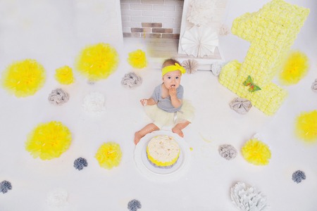 a little girl eats cake with her hands on the bacfground of fireplace. The baby was covered in food. birthday partyの写真素材