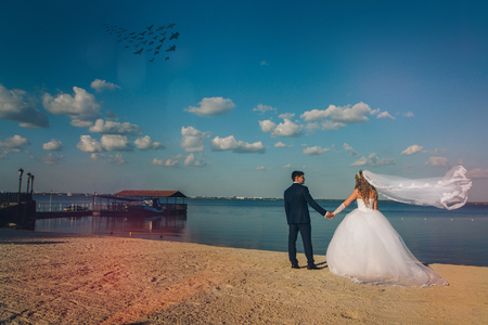 Wedding couple on the nature is hugging each other. Beautiful model girl in white dress. Man in suit. Beauty bride with groom. Female and male portrait. Woman with lace veil. Lady and guy outdoorsの写真素材
