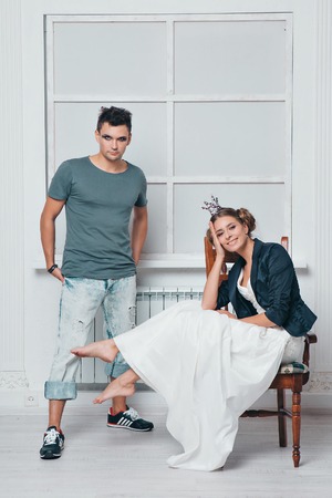 a man with makeup stands next to a girl in a crown who sits on a chair in white dressの写真素材