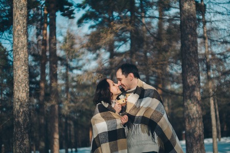 man and woman wrapped in a blanket and holding cups in the background of winter forestの写真素材