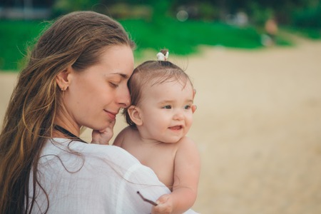 baby in the arms of the mother. Woman holding a child on beach and tropical vegetation background
