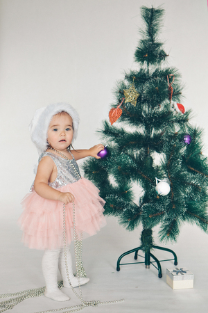 a little girl in a dress adorns the Christmas tree on a white backgroundの写真素材