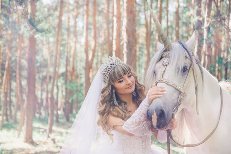 bride stroking the white unicorn on the forest backgroundの写真素材