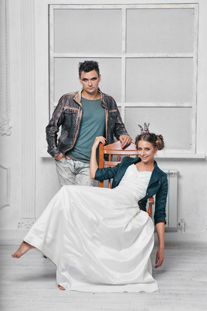 a man with makeup in a leather jacket stands next to a girl in a crown who sits on a chairの写真素材
