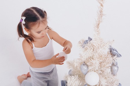 a little girl with two tails decorates a Christmas tree on a white backgroundの写真素材