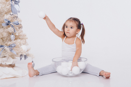 a little girl with two tails decorates a Christmas tree on a white backgroundの写真素材