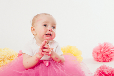 a little girl eats cake with her hands. The baby was covered in food. isolated white background. birthday partyの写真素材