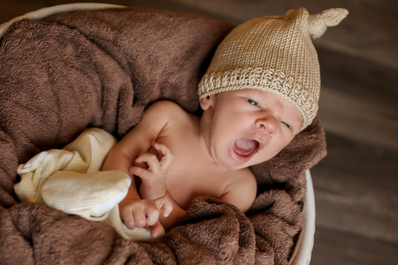 a small child in a basket sleeps in a warm knitted hat with a pompom yawnsの写真素材