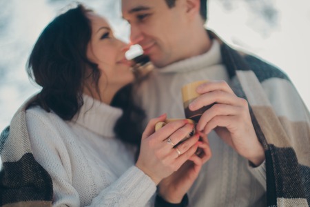 man and woman wrapped in a blanket and holding cups in the background of winter forestの写真素材