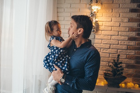 a little girl on the hands of father near a garland and a small Christmas treeの写真素材