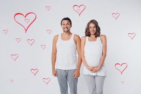 Family portrait: the husband embraces the pregnant wife on a white background. pregnant couple in love. Valentines day heart patternの写真素材