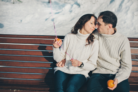 Valentine's day: a couple in love sitting on a bench in a winter forest with an orange balloon and orangesの写真素材