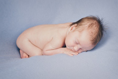 naked newborn baby sleeping curled up in a ballの写真素材