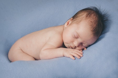 naked newborn baby sleeping curled up in a ballの写真素材