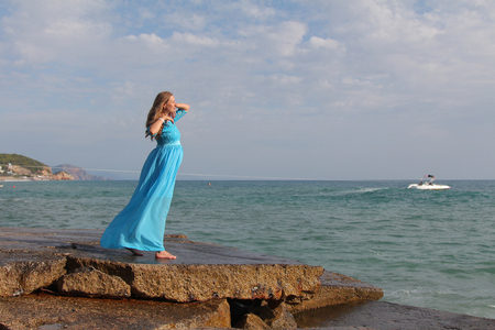 pregnant girl in blue dress on stones by the seaの写真素材