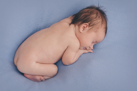 naked newborn baby sleeping curled up in a ballの写真素材