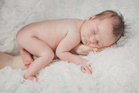 naked newborn baby sleeping curled up in a ballの写真素材