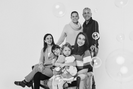 group of people on a white background: adults and children with toys sitting on the same couch