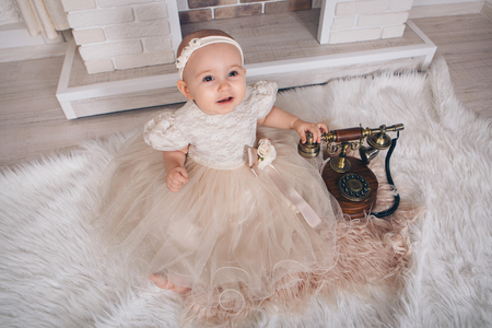 a little girl in a white dress sitting by the fireplace next to an old phoneの写真素材