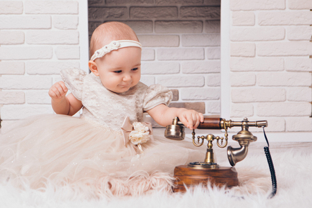 a little girl in a white dress sitting by the fireplace next to an old phoneの写真素材