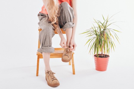 women's feet in linen clothes and shoes next to a flower on a white backgroundの写真素材