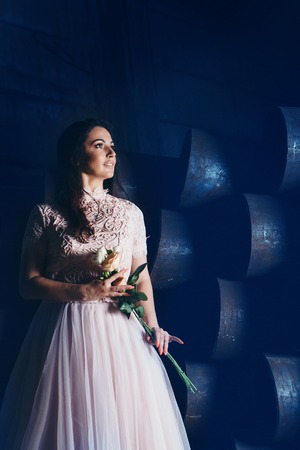 March 8: beautiful girl in a light dress with bouquet of flowers among metal pipesの写真素材