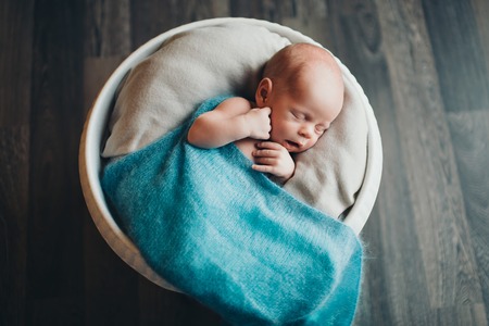 newborn baby wrapped in a blanket sleeping in a basketの写真素材