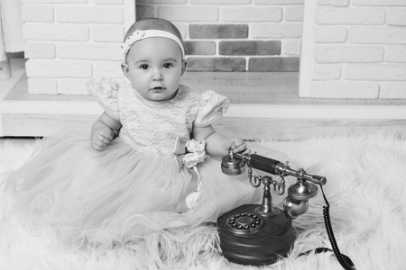 a little girl in a white dress sitting by the fireplace next to an old phoneの写真素材