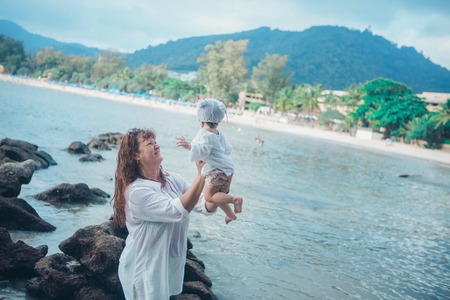 baby in the arms of the mother. Woman holding a child on the sea background. Travelの写真素材