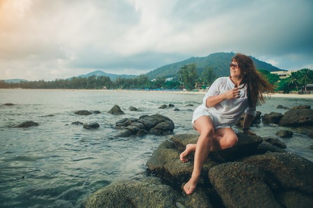 a woman in sun glasess on a rock looking into the distance against the seaの写真素材