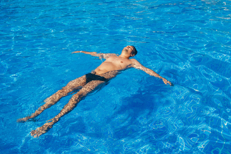 tanned man on vacation swimming in the poolの写真素材