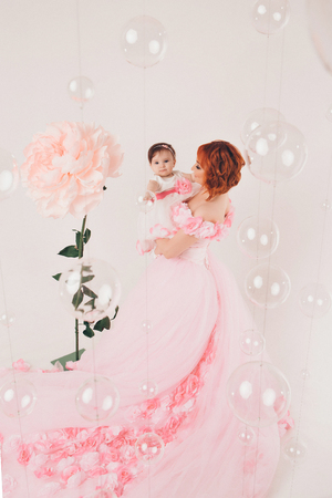 the child in the arms of his mother in a pink dress of flowers. A woman with a child in her arms on a white background, isolatedの写真素材