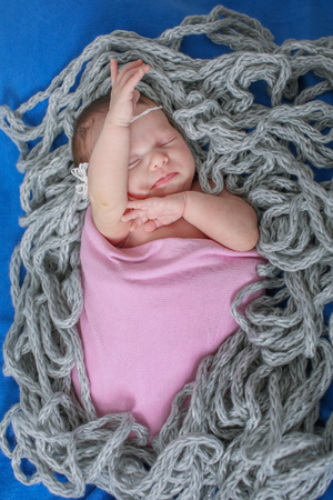 naked newborn baby sleeps curled up in a ball in a braided ropeの写真素材