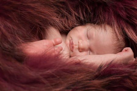 A little child in a red fur lies . Portrait of newbornの写真素材