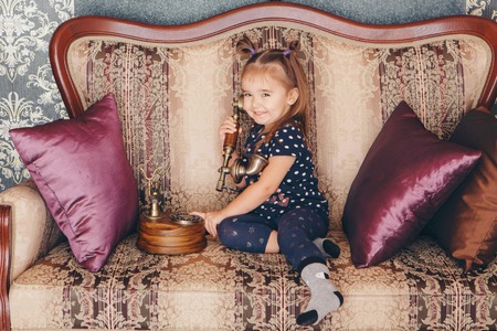 little girl sitting on the couch talking on an old phoneの写真素材