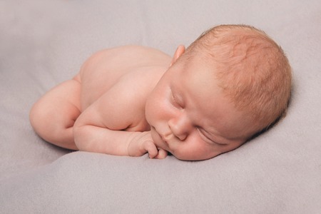 naked newborn baby sleeping curled up in a ballの写真素材