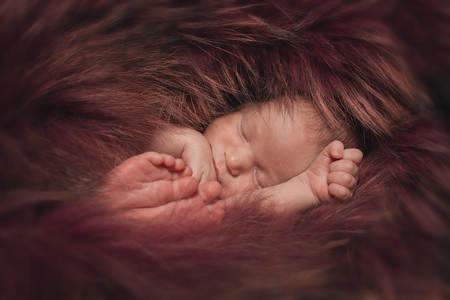 A little child in a red fur lies . Portrait of newbornの写真素材