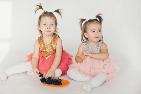 two little girls eating grapes sitting on the floor on a white backgroundの写真素材
