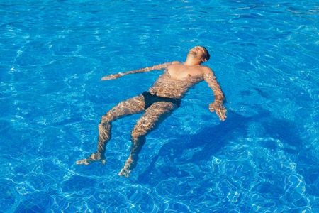 tanned man on vacation swimming in the poolの写真素材