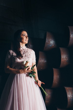 March 8: beautiful girl in a light dress with bouquet of flowers among metal pipesの写真素材