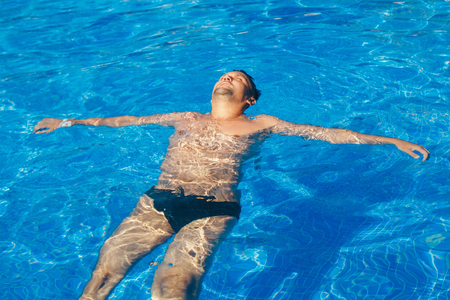 tanned man on vacation swimming in the poolの写真素材