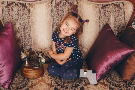 little girl sitting on the couch talking on an old phoneの写真素材