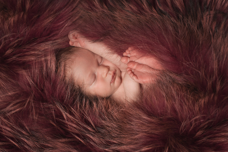 A little child in a red fur lies . Portrait of newbornの写真素材