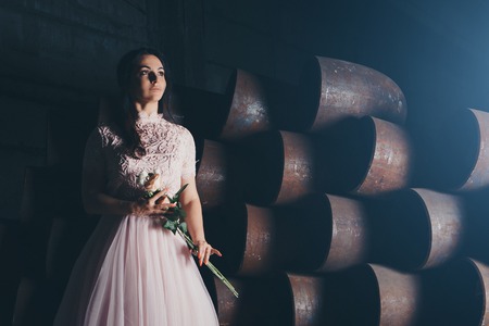 March 8: beautiful girl in a light dress with bouquet of flowers among metal pipesの写真素材