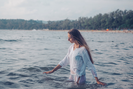 girl with long hair in white shirt posing in waterの写真素材