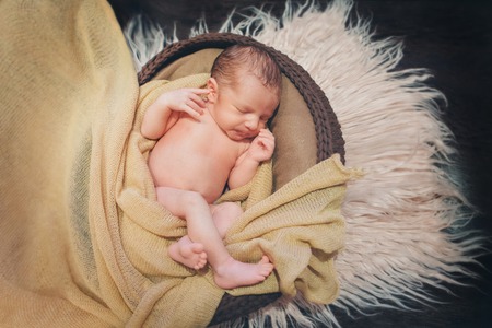 naked newborn baby sleeping curled up in a ballの写真素材