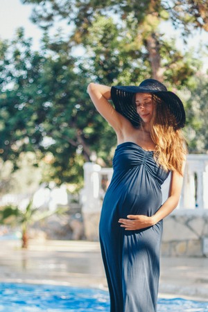 pregnant woman with long hair in blue dress posing in waterの写真素材