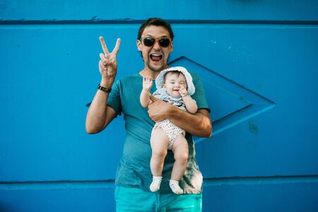 Dad with glasses holding a baby on a blue background and shows a hippie sign: worldの写真素材
