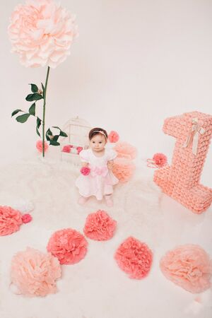 Birthday celebration: girl sitting on the floor among the numbers 1, artificial flowers and bird cageの写真素材